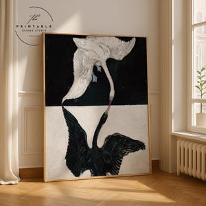 Puede incluir: Una impresión artística enmarcada que presenta dos cisnes, uno blanco y otro negro, enfrentados. La obra de arte está dividida en secciones en blanco y negro. El cisne blanco está arriba y el cisne negro abajo. El logotipo de Printable Design Studio está en la esquina superior izquierda.