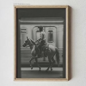 May include: Black and white framed print of a cowboy riding a horse past a speeding train. The cowboy wears a hat and is seated on a saddle. The train is blurred, suggesting motion. The print is in a wooden frame.