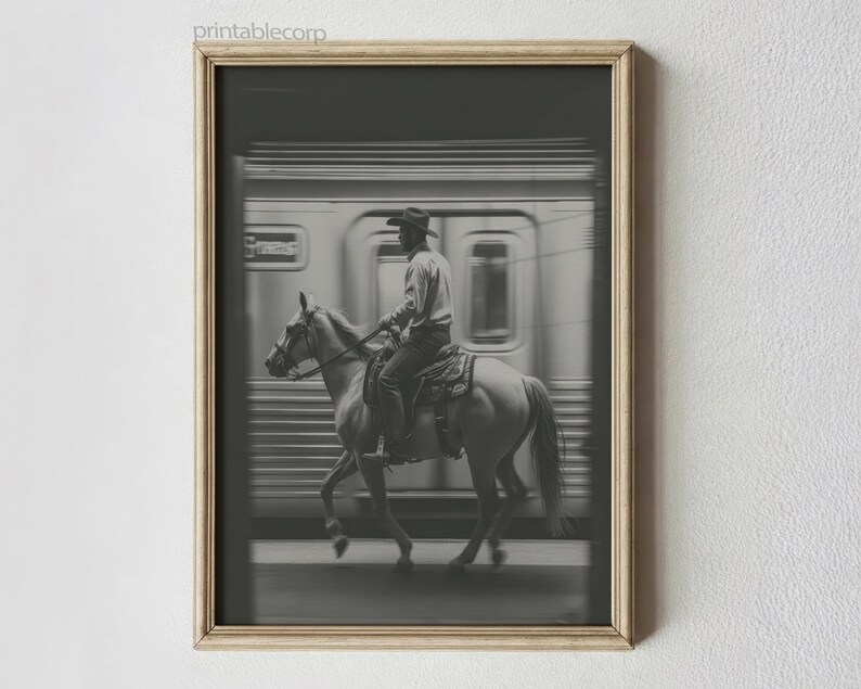 May include: Black and white framed print of a cowboy riding a horse past a speeding train. The cowboy wears a hat and is seated on a saddle. The train is blurred, suggesting motion. The print is in a wooden frame.