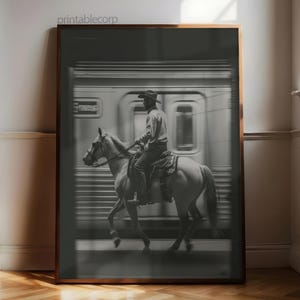 May include: Black and white framed print featuring a cowboy riding a horse in front of a blurred train. The print has a sepia tone and the text "printablecorp" is in the top left corner.
