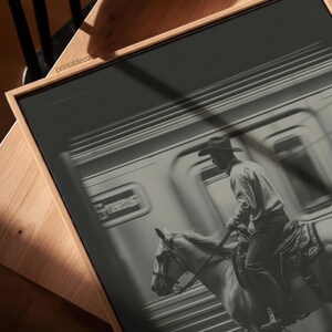 May include: Black and white framed print featuring a cowboy on horseback, riding past a train. The cowboy wears a hat and is riding a light-colored horse. The print has a wooden frame and the text "printable.com" is visible.