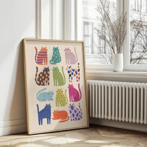 Puede incluir: Una impresi&oacute;n art&iacute;stica enmarcada con una cuadr&iacute;cula de ilustraciones de gatos coloridos. Cada gato tiene un patr&oacute;n y color &uacute;nicos, incluyendo rayas naranjas, lunares azules y manchas rosas. La obra de arte se exhibe en una habitaci&oacute;n con una ventana y un radiador.