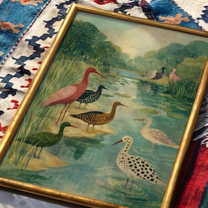 Puede incluir: Pintura enmarcada que representa un sereno paisaje acu&aacute;tico con diversas especies de aves. La obra de arte muestra aves en tonos de rosa, verde, negro y blanco, sobre un fondo de agua y exuberante vegetaci&oacute;n. El marco es dorado.