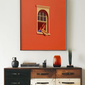 May include: A framed art print featuring a minimalist illustration of a window with a person's legs extending out. The artwork is set against a vibrant orange background. The print is above a wooden dresser.