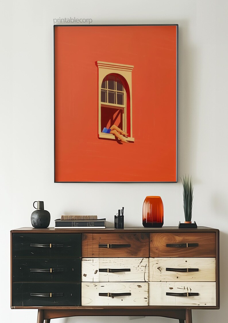 May include: A framed art print featuring a minimalist illustration of a window with a person's legs extending out. The artwork is set against a vibrant orange background. The print is above a wooden dresser.