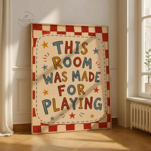 Può includere: Un poster incorniciato con la scritta "THIS ROOM WAS MADE FOR PLAYING" in lettere colorate. Il poster ha uno sfondo color crema con un bordo a scacchi rosso e bianco e accenti di stelle.