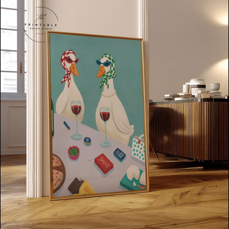 May include: A framed art print featuring two white geese wearing sunglasses and scarves, enjoying wine. The table includes pizza, cheese, and a box labeled "SAVVY." The background is a light teal color.
