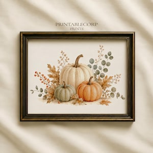 May include: A framed art print featuring the text PRINTABLECORP PRINTS above a watercolor illustration of three pumpkins in cream, sage green, and orange, surrounded by autumn leaves, berries, and eucalyptus branches on a light background.