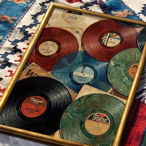May include: A framed collection of vintage vinyl records. The records are in various colors, including red, blue, green, and black, with labels featuring text like "Soul & Jazz Gems" and "Vintage Vinyl Hits." The frame is gold-colored.