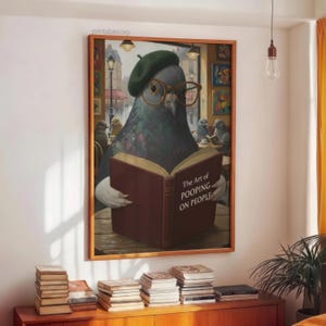 May include: A framed print featuring a pigeon wearing glasses and a beret, reading a book titled "The Art of Pooping on People." The artwork has a humorous theme, with other pigeons in the background. The print is displayed above a wooden cabinet with stacks of books.