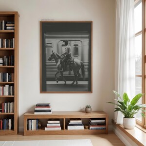 May include: Black and white framed print of a cowboy riding a horse in front of a train. The image is in a room with a wooden bookshelf, a wooden bench with books, and a window with white curtains.
