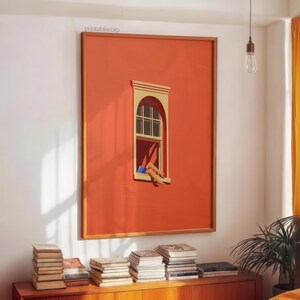 May include: A framed art print featuring a vibrant orange wall with a window. The window has a beige frame and a person's legs are visible, resting outside. The artwork is displayed above a wooden cabinet with stacks of books.