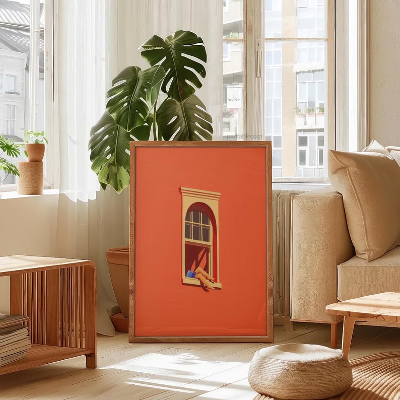 May include: A framed art print featuring an orange background with a window illustration. The window is detailed with a yellow frame and a person's legs hanging out. The artwork is displayed in a living room setting with a wooden side table and a large green plant.