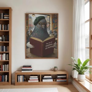 May include: A framed print featuring a pigeon wearing a beret and glasses, reading a book titled "The Art of Pooping on People." The artwork has a humorous theme, with the pigeon in a cafe setting.
