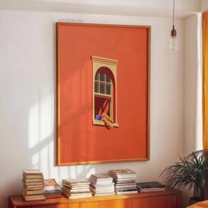 May include: A framed art print featuring a vibrant orange wall with a window. The window has a beige frame and a person's legs are visible, resting outside. The artwork is displayed above a wooden cabinet with stacks of books.