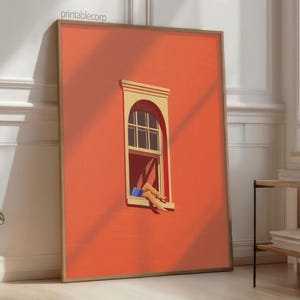 May include: A framed art print featuring a vibrant orange wall with a window. The window has a beige frame and a person's legs are visible, wearing blue shorts. The artwork is leaning against a white wall.