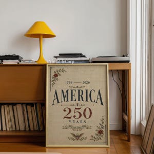 Pu&ograve; includere: Una stampa incorniciata con la scritta "AMERICA 250 YEARS" in blu navy e rosso, con decorazioni floreali. La stampa &egrave; esposta su un mobile in legno, accanto a una lampada gialla e un giradischi.