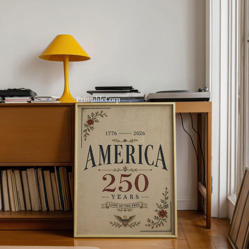 Pu&ograve; includere: Una stampa incorniciata con la scritta "AMERICA 250 YEARS" in blu navy e rosso, con decorazioni floreali. La stampa &egrave; esposta su un mobile in legno, accanto a una lampada gialla e un giradischi.