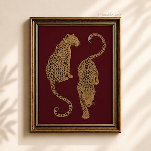 Puede incluir: Una lámina de arte mural enmarcada que muestra dos leopardos de color dorado sobre un fondo burdeos intenso. Un leopardo está sentado de perfil mientras el otro camina hacia adelante. El marco es de oro metálico oscuro con acabado texturizado.