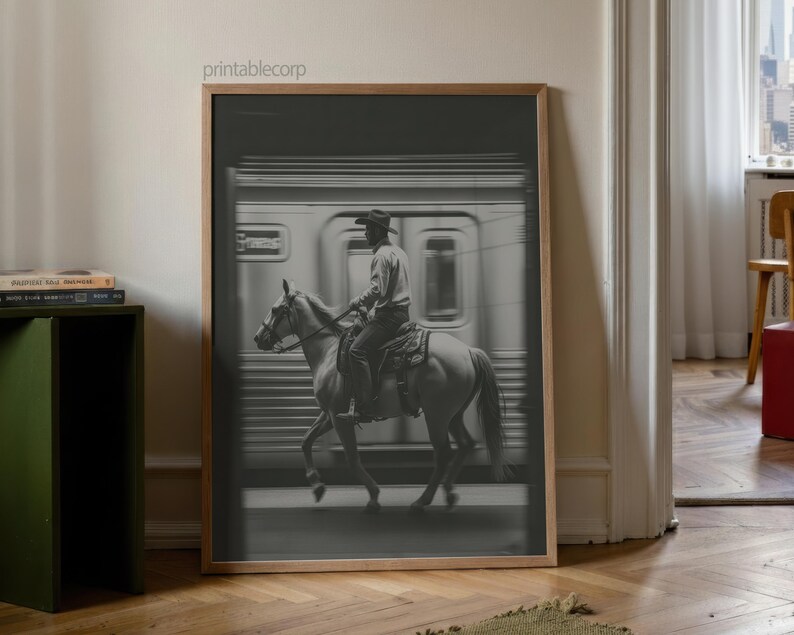 May include: Black and white framed print of a cowboy riding a horse in front of a subway train. The cowboy wears a hat and is seated on a saddle. The image has a vintage, cinematic feel.
