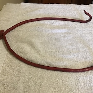 May include: A red metal hook with a curved handle. The hook is made of a single piece of metal and has a smooth finish.