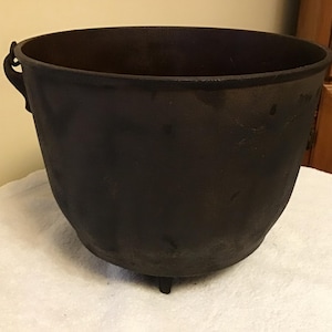 May include: A large, black cast iron pot with a single handle and three short legs. The pot is made of heavy-duty cast iron and has a rustic, vintage look.