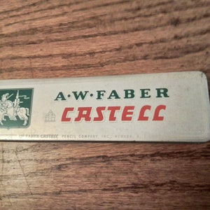 May include: A white metal tin with green and red lettering. The tin says "A.W. FABER CASTEEL" and "FABER-CASTEEL PENCIL COMPANY, INC., NEWARK, N.J.". A knight on horseback is pictured in the upper left corner.