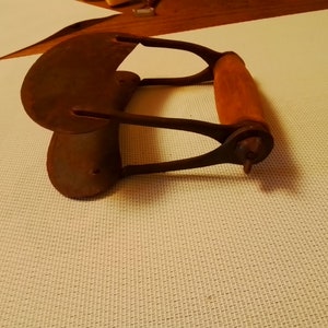 May include: A vintage, rusty metal butter churn with a wooden handle. The churn is shaped like a half-circle and has a pointed end.