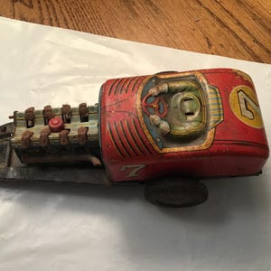 May include: Vintage red and yellow toy race car with the number 4 on the side. The toy car has a detailed engine and driver's seat. The car is made of metal and shows signs of wear.