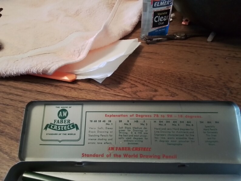 May include: A vintage metal tin box with a green and white label that reads "A.W. Faber-Castell Standard of the World Drawing Pencil". The label explains the different degrees of hardness for drawing pencils, from 7B to 9H.