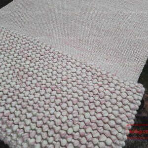 May include: A close-up of a pink and white fluffy rug with a textured, bubble-like design. The rug is made of wool and has a soft, comfortable feel. The text "Red Rugs Creations" is visible in the lower right corner of the image.