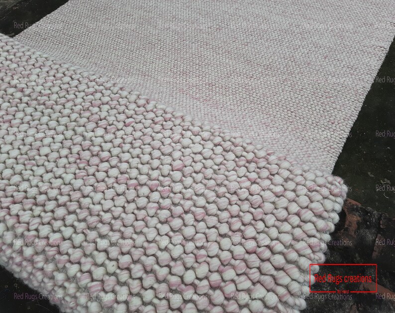 May include: A close-up of a pink and white fluffy rug with a textured, bubble-like design. The rug is made of wool and has a soft, comfortable feel. The text "Red Rugs Creations" is visible in the lower right corner of the image.