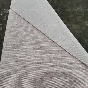 May include: A close-up of a white and pink woven rug with a textured surface. The rug is folded in half, revealing the underside of the rug.