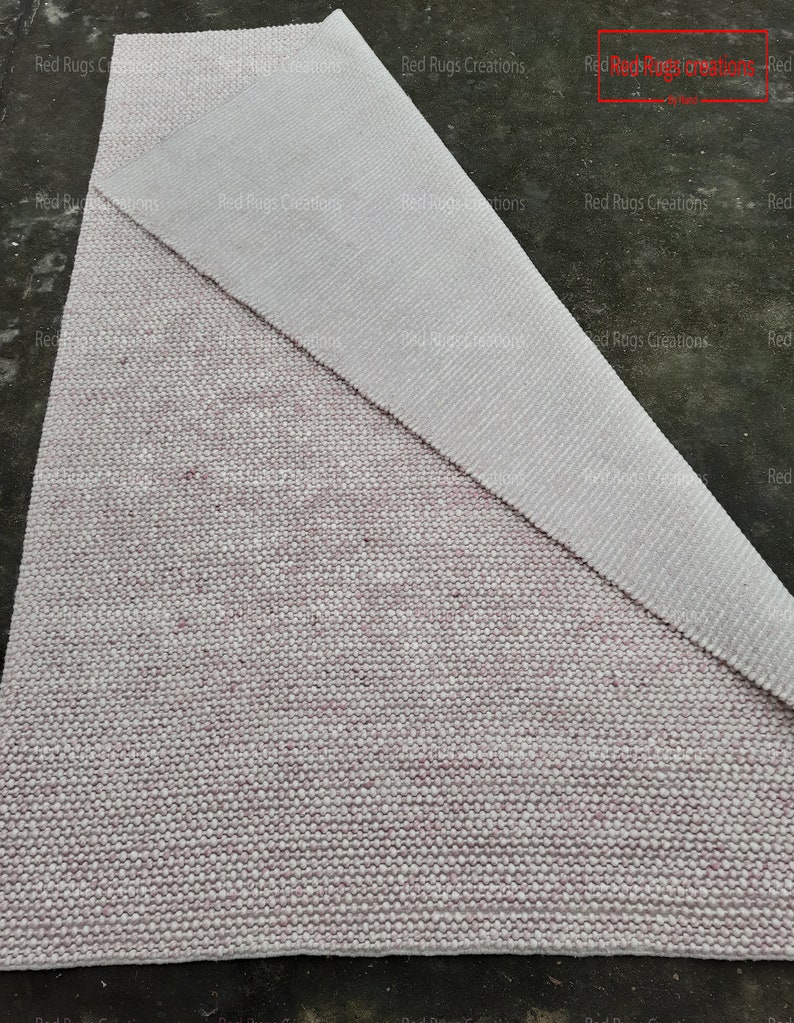 May include: A close-up of a white and pink woven rug with a textured surface. The rug is folded in half, revealing the underside of the rug.