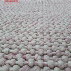 May include: Close-up of a white and pink fluffy rug made of small, round balls of yarn. The rug is handmade and has a textured surface.