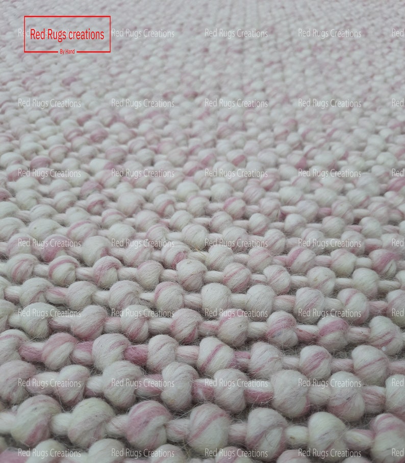 May include: Close-up of a white and pink fluffy rug made of small, round balls of yarn. The rug is handmade and has a textured surface.