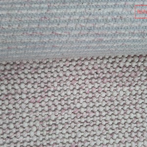May include: Close-up of a white and pink woven rug with a textured, bumpy surface. The rug is made of small, round balls of yarn. The text "Red Rugs creations" is visible in the top right corner of the image.