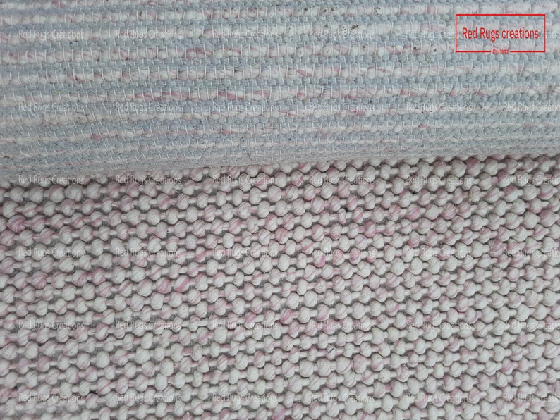 May include: Close-up of a white and pink woven rug with a textured, bumpy surface. The rug is made of small, round balls of yarn. The text "Red Rugs creations" is visible in the top right corner of the image.