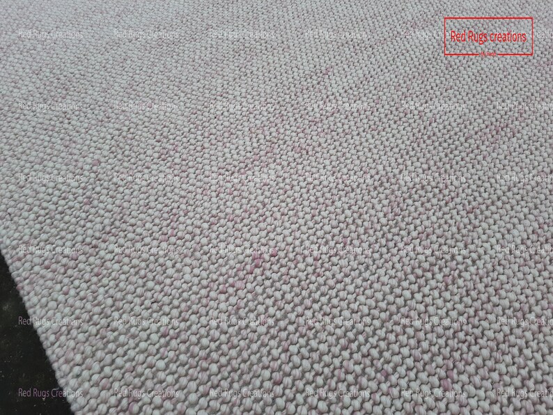 May include: Close-up of a white and pink textured rug with a woven design. The rug is made of small, round balls of yarn. The text "Red Rugs creations" is visible in the top right corner of the image.