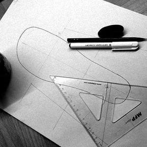 以下が含まれることがあります： 白い紙の上に定規、鉛筆、ペンが置かれたデザインプロジェクトの白黒写真。デザインは靴の簡単なアウトラインです。