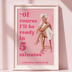 May include: A framed wall art print with a pink background featuring a retro-style illustration of a person wrapped in a white towel sitting on a wooden stool. The text reads: Of course I'll be ready in 5 minutes, A FICTIONAL NOVEL BY ME.