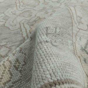 Könnte beinhalten: Nahaufnahme eines beigefarbenen und hellbraunen Teppichs mit einem detaillierten, traditionellen Muster. Der Teppich hat ein weiches, strukturiertes Aussehen mit einem gerollten Rand, der das komplizierte Design und die Farbvariationen zeigt. Das Design des Teppichs umfasst florale und geometrische Elemente.