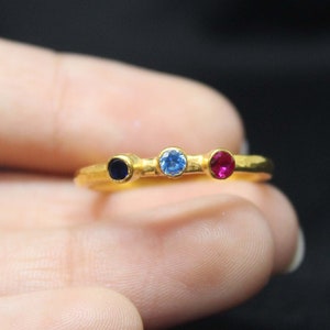 May include: A gold ring with three small gemstones: a blue sapphire, a light blue topaz, and a red ruby.
