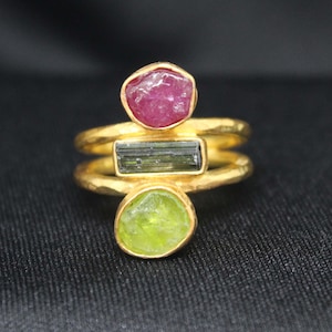 May include: Gold ring with three gemstones: a pink ruby, a green tourmaline, and a green peridot.