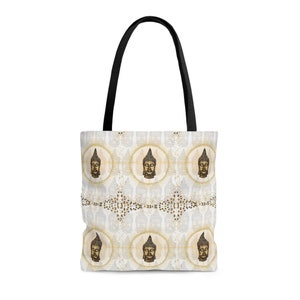 May include: A white tote bag with a repeating pattern of gold Buddha faces on a white background. The bag has black handles.