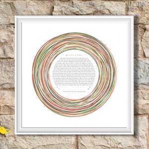 May include: A square white frame containing a circular artwork with Hebrew text in the center. The text is surrounded by concentric, hand-drawn style rings in shades of red, green, and brown. The names Abigail and Ezra are printed at the top.
