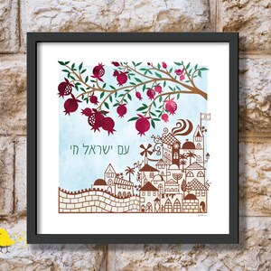 May include: A framed print of a stylized illustration of a city with a pomegranate tree above it. The city is depicted in brown and the tree is green with red pomegranates. The text "עם ישראל" is written in Hebrew below the tree.