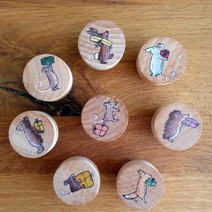 Könnte beinhalten: Acht Holzornamente, jedes mit einem anderen Tier, das ein Geschenk trägt. Die Tiere sind ein Kaninchen, eine Maus, ein Igel, ein Fuchs und drei verschiedene Mäuse. Die Ornamente sind in verschiedenen Farben bemalt, darunter Braun, Grau, Rosa und Gelb.