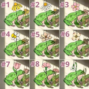 May include: Nine stained glass frog suncatchers, each with a different flower. The frogs are green with pink bellies, and the flowers include a daisy, daffodil, and tulip. Each suncatcher is labeled with a number from 1 to 9.