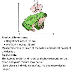 May include: A handmade stained glass frog with a pink and white orchid flower. The frog is green with pink accents, and the design measures 5.9 inches (15 cm) high and 5.1 inches (13 cm) wide. The frog is suspended by a chain.
